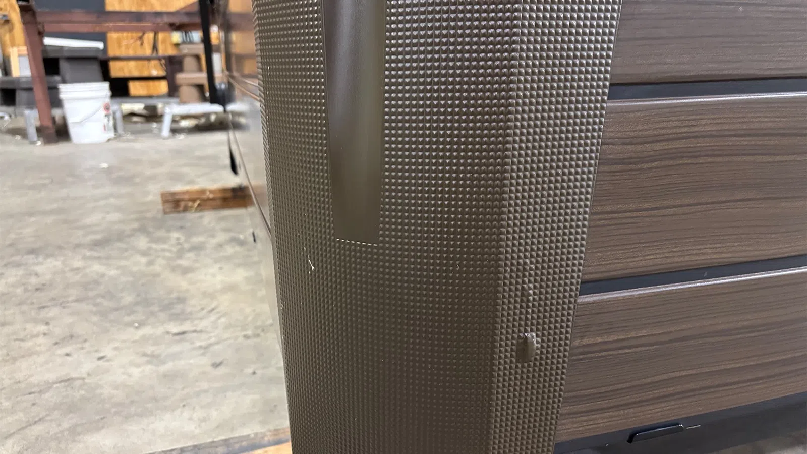 Close-up of textured brown luggage corner with a handle against a warehouse floor background.