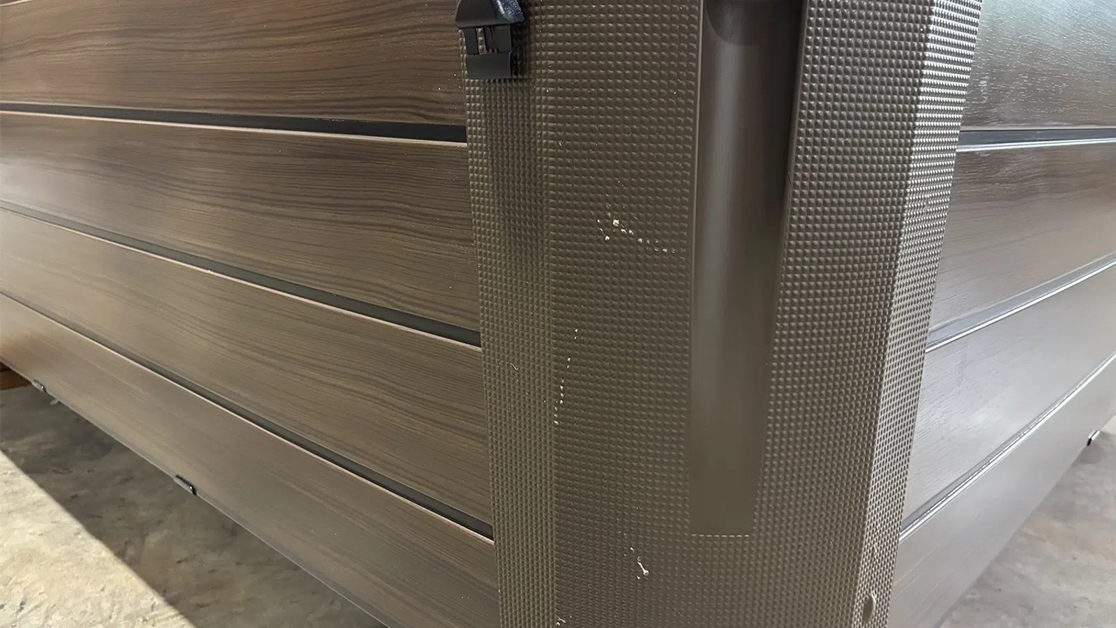 Close-up of a textured dark brown hard case with a black handle and wood-patterned panels on a concrete floor.