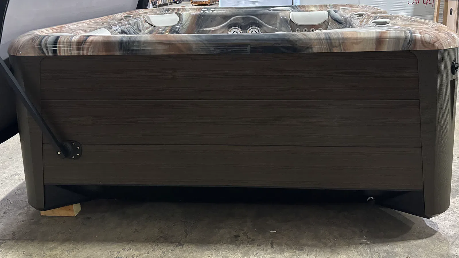 Modern outdoor hot tub with wood-paneled exterior and marble-patterned interior in warehouse setting