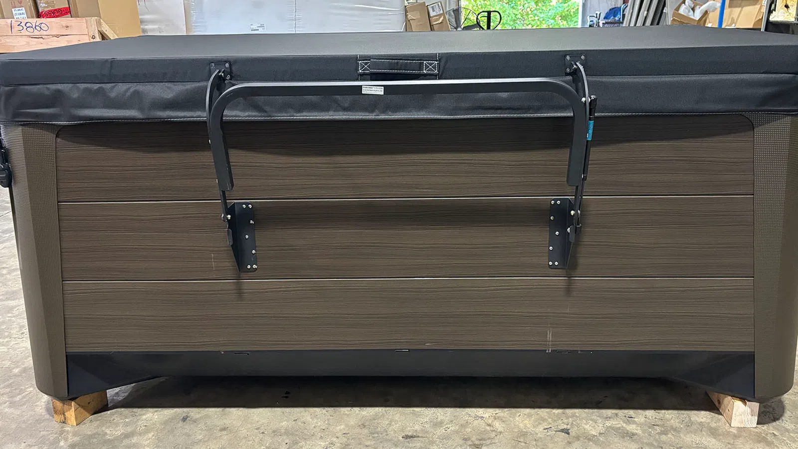 Back view of a rectangular hot tub with dark wood paneling and a black cover in a warehouse setting