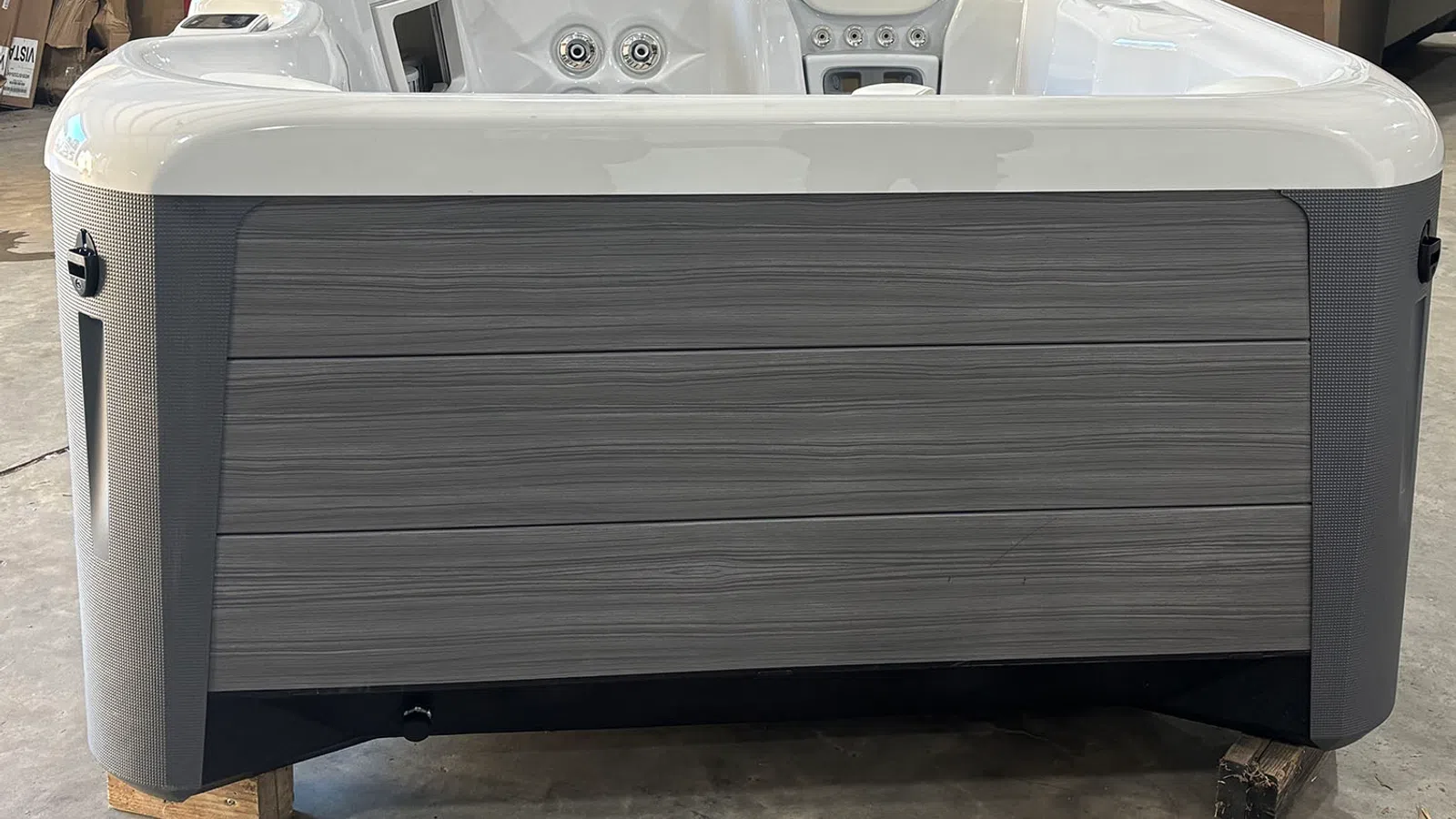 Modern gray and white outdoor hot tub with wood-like paneling and multiple jets on the side and interior.