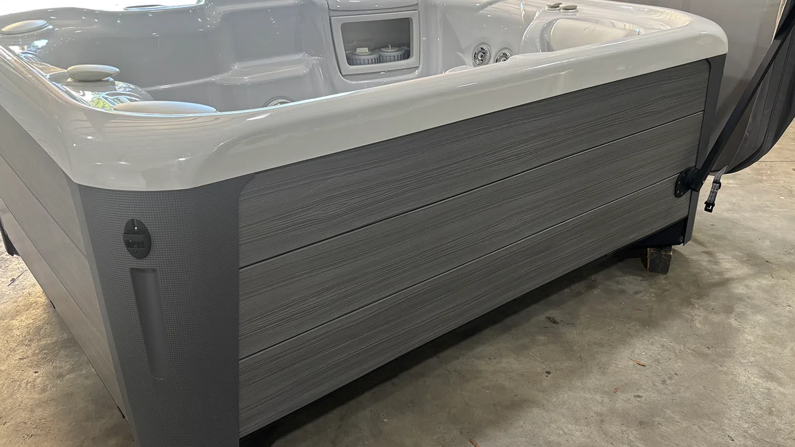 Modern gray and white hot tub with built-in jets and seating on a concrete floor indoors.