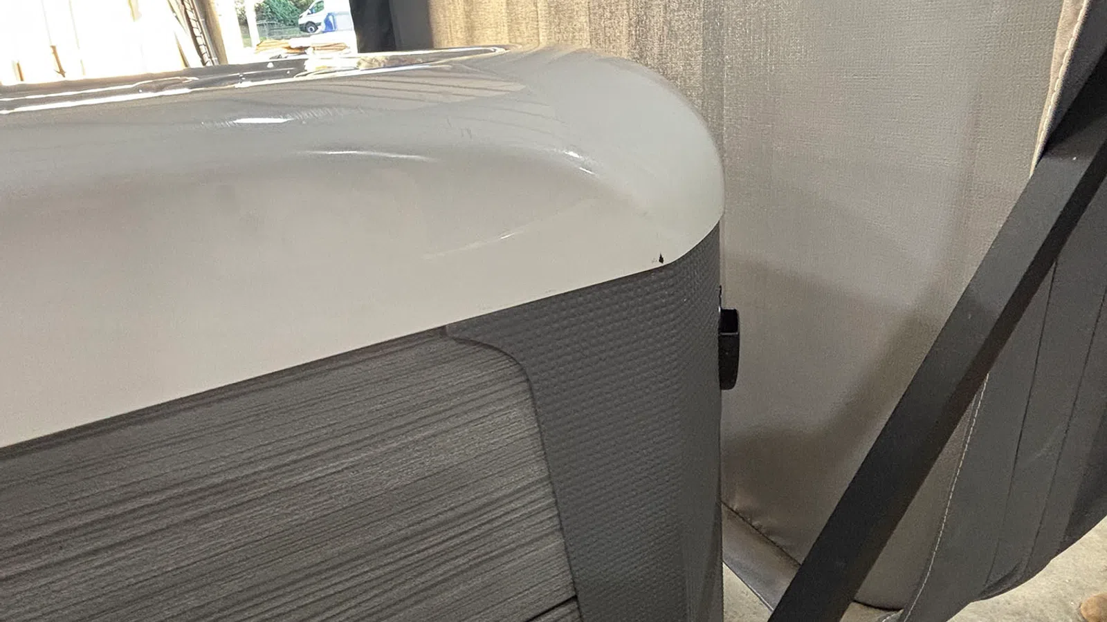 Close-up of a modern hot tub corner with white lid and textured gray side panel near curtains indoors.