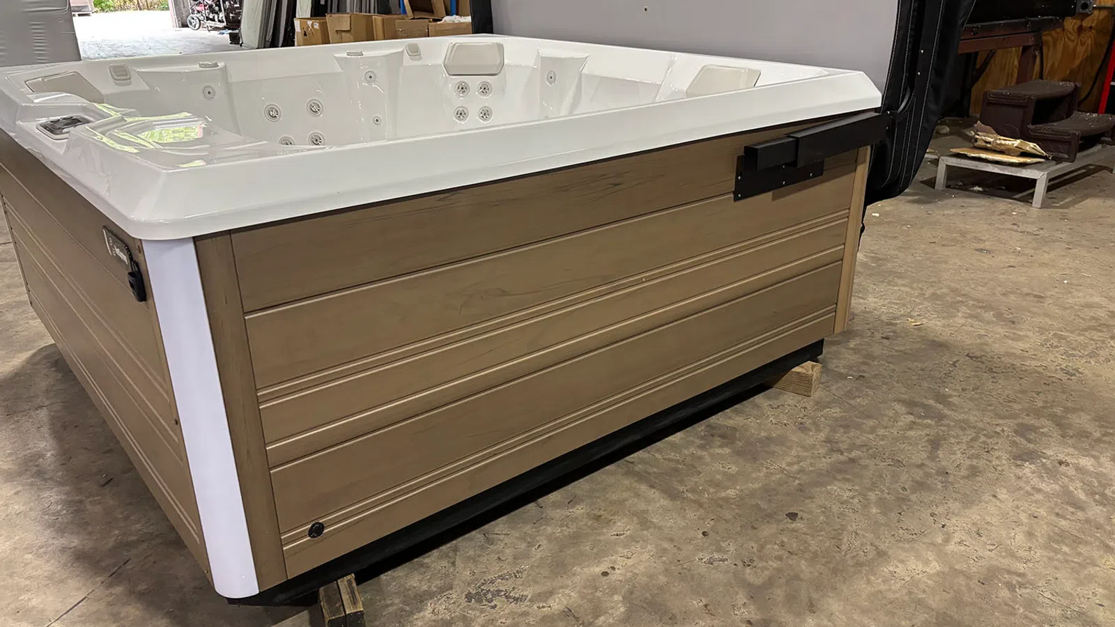 Wood-paneled hot tub with white interior and multiple jets on concrete floor in warehouse space