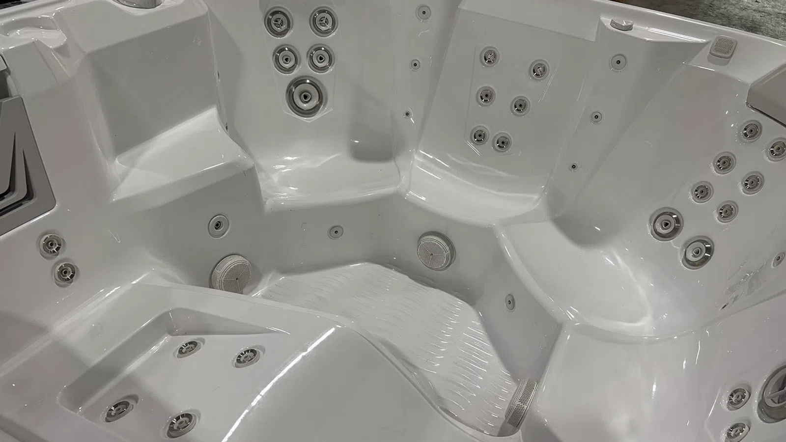 Empty white hot tub spa with multiple jet nozzles and built-in seats in a showroom setting.