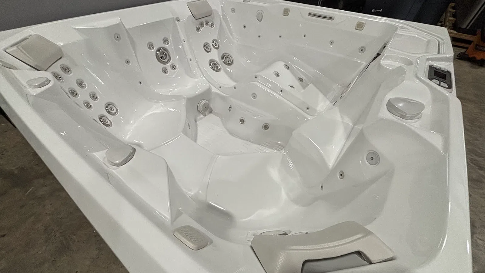 Empty white luxury hot tub with built-in jets and headrests in a showroom setting