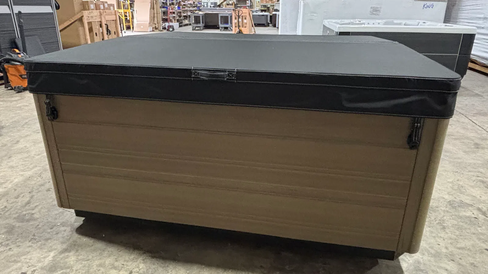 Rectangular hot tub with a closed black cover in an indoor warehouse setting