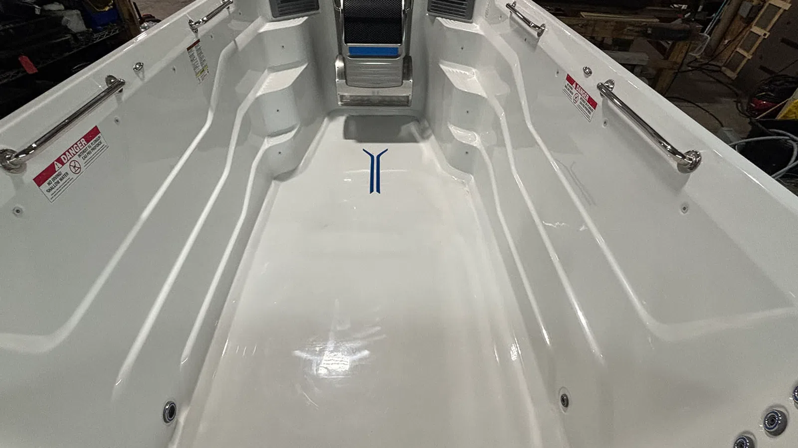 Empty white swim spa with built-in seats, handrails, and control panel in industrial setting