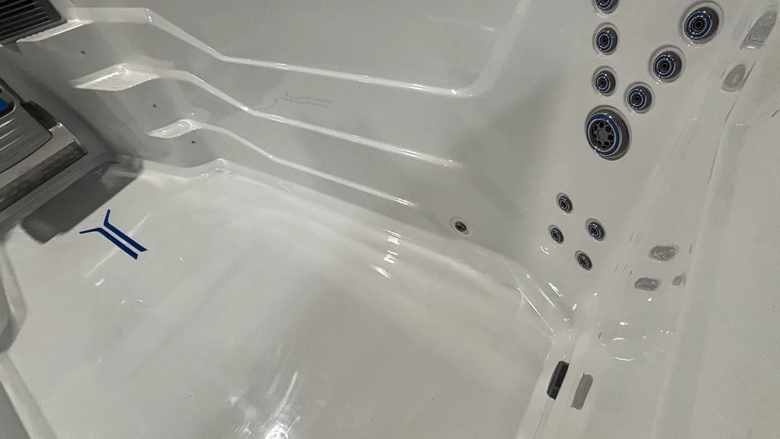 Empty white jacuzzi tub with multiple water jets and a blue logo inside the tub basin