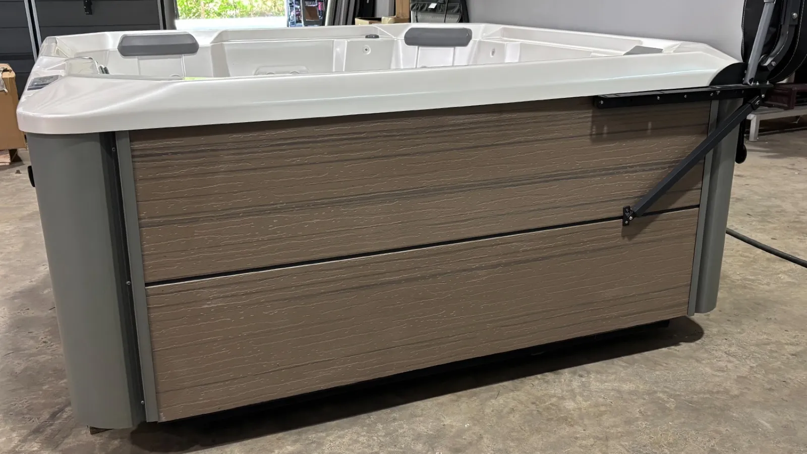 Modern rectangular hot tub with wood-like paneling and white interior seats in an indoor setting.