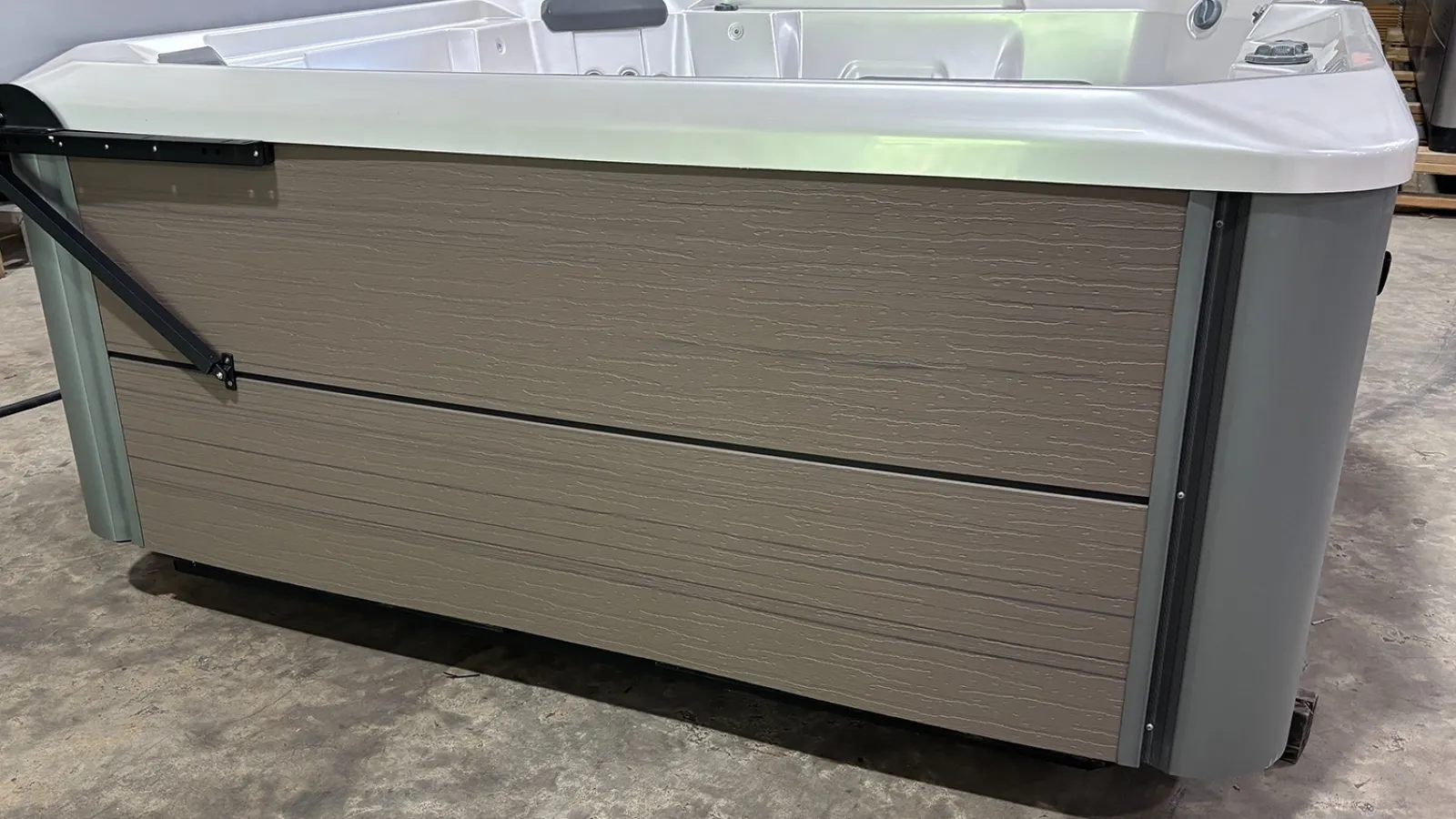 Modern white and beige hot tub with textured side panels on concrete floor in an indoor setting