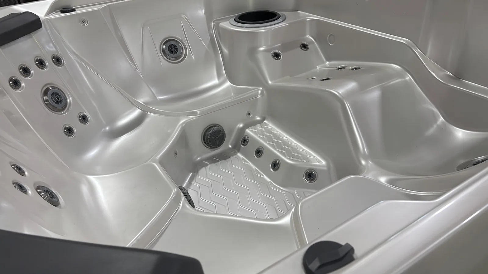 Interior of a modern white hot tub showing multiple seating areas and water jet nozzles for hydrotherapy.
