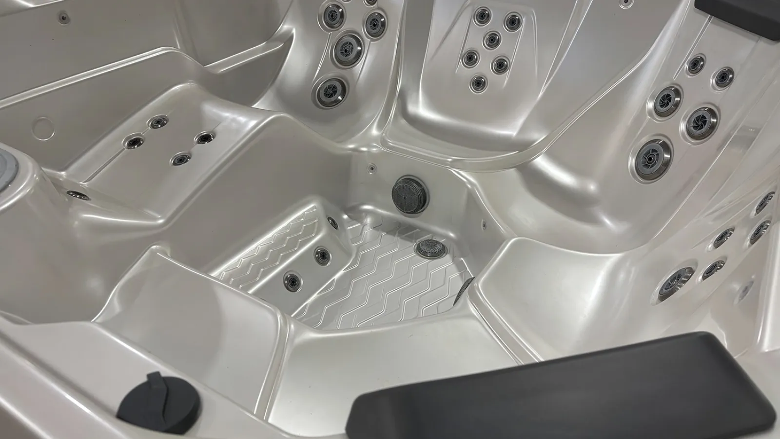 Empty silver hot tub with multiple jets and ergonomic seats in a modern spa setting.