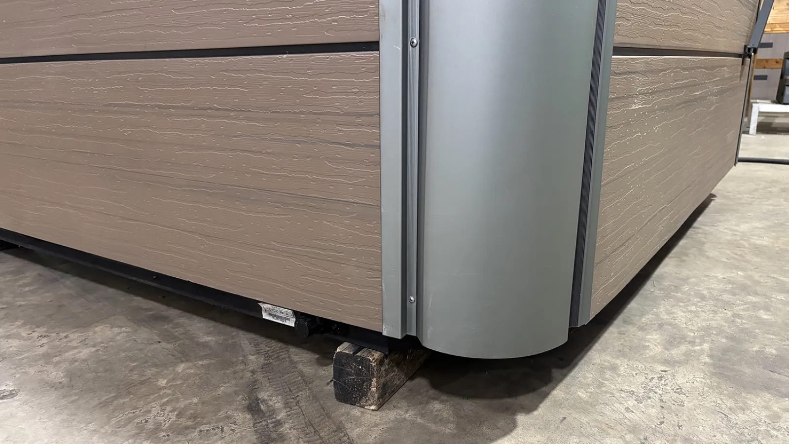 Close-up of a corner of a beige wooden structure with a curved metallic edge on a concrete floor.