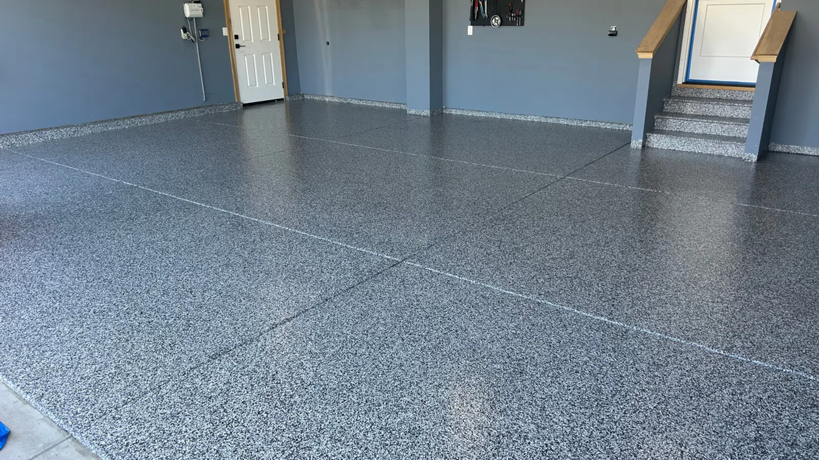Clean garage with freshly installed speckled epoxy floor coating and organized blue walls with shelves and doors.