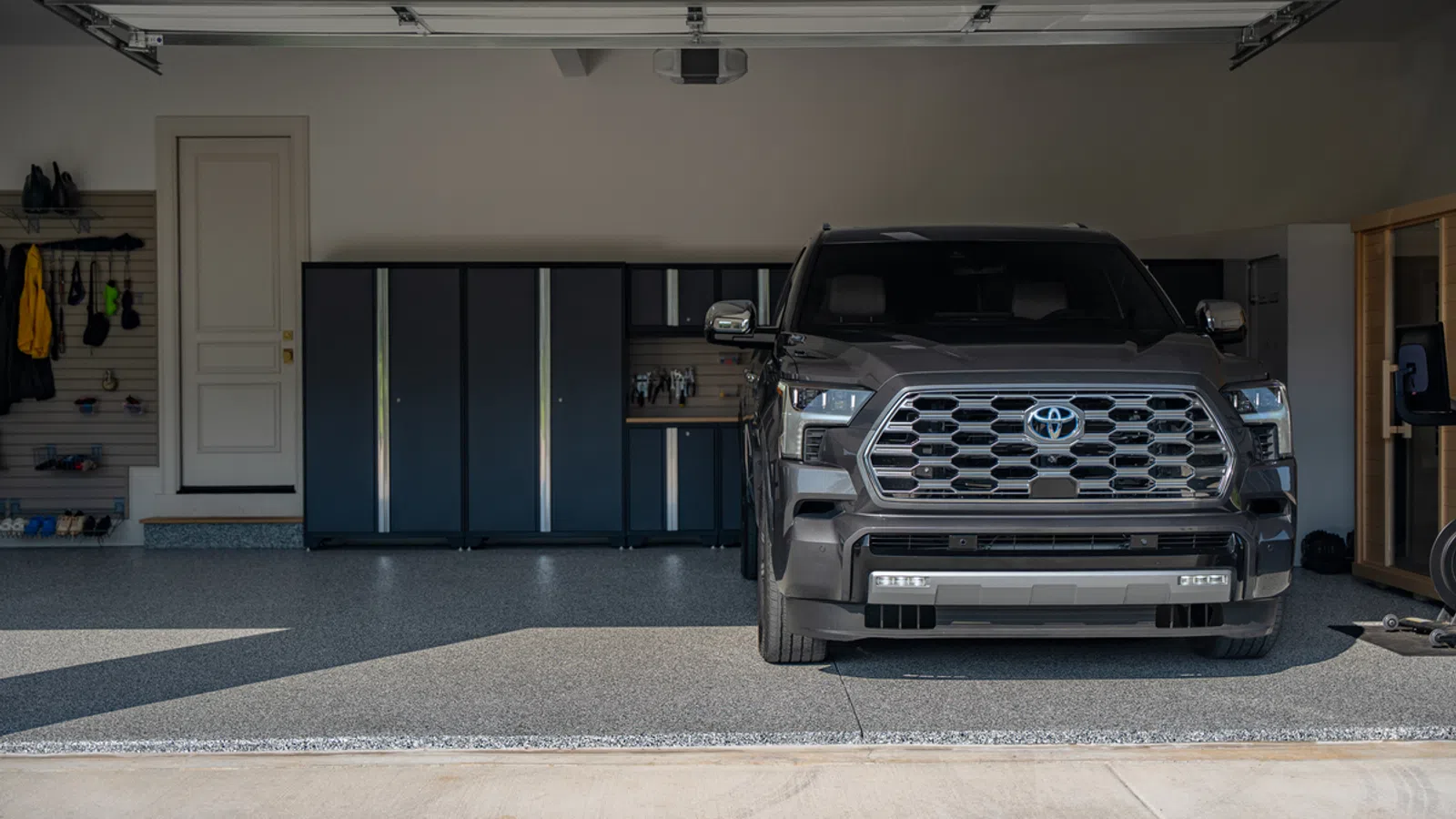 Black Toyota pickup truck parked inside a clean, organized garage with storage cabinets and tools on wall.