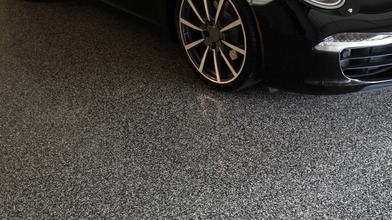 Close-up of black sports car tire and sleek front bumper on speckled epoxy garage floor