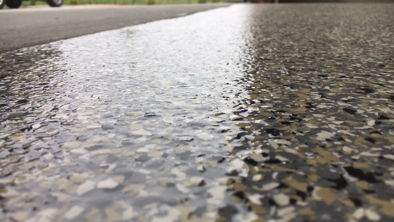 Close-up of a glossy epoxy-coated garage floor with multicolored flakes and a blurred car in the background.