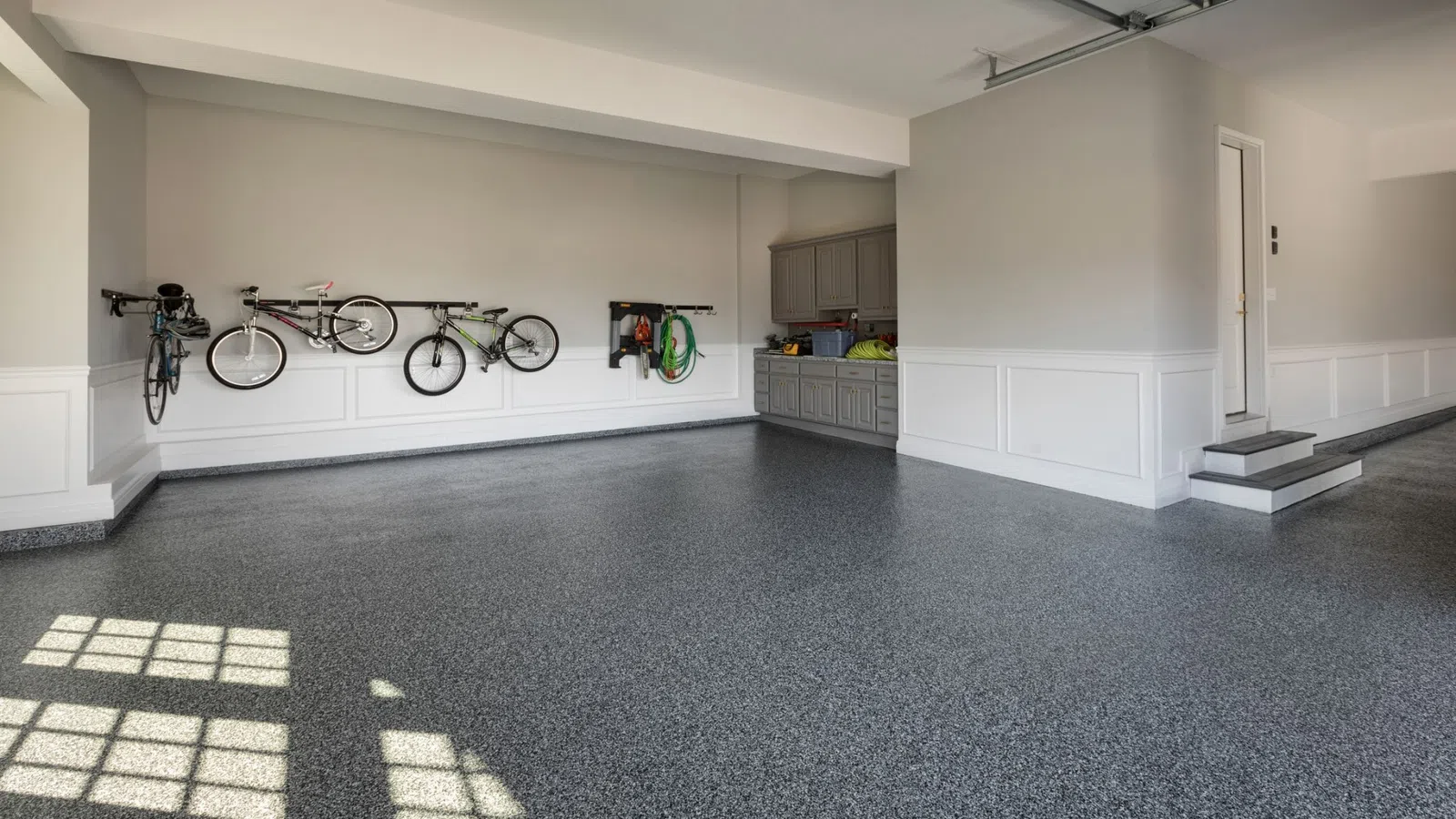 Spacious clean garage with speckled floor, wall-mounted bikes, storage cabinets, and natural window light.