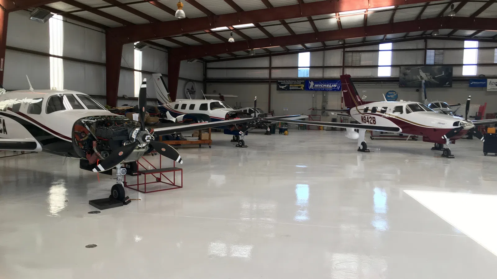 Small propeller airplanes parked inside a spacious, well-lit aircraft hangar with high ceilings and reflective floors.