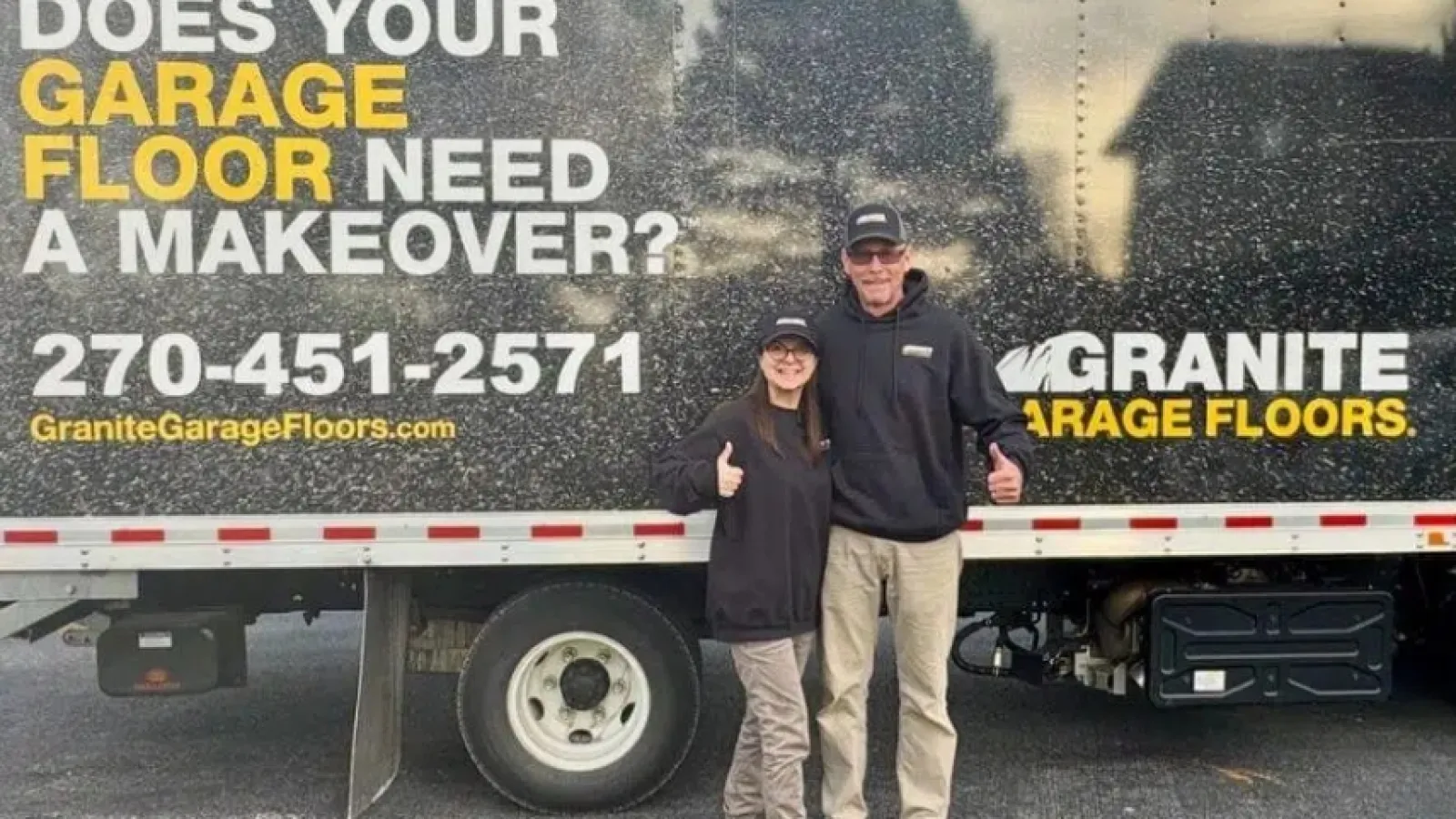 Two people standing in front of a Granite Garage Floors truck advertising garage floor makeovers and contact info.