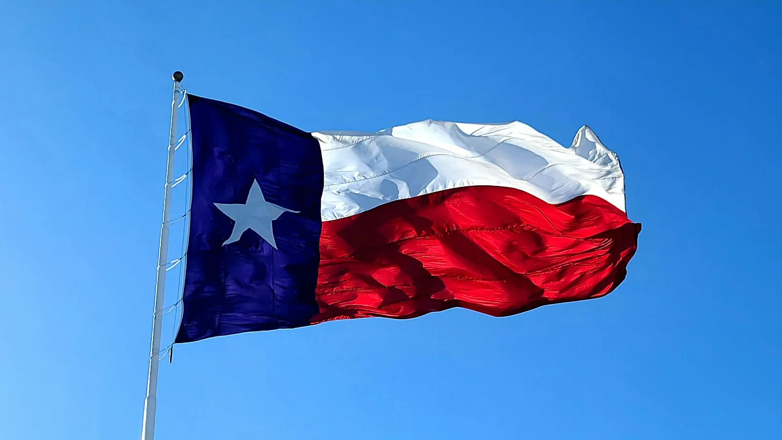 Texas state flag with a lone star waving against a clear blue sky on a flagpole.