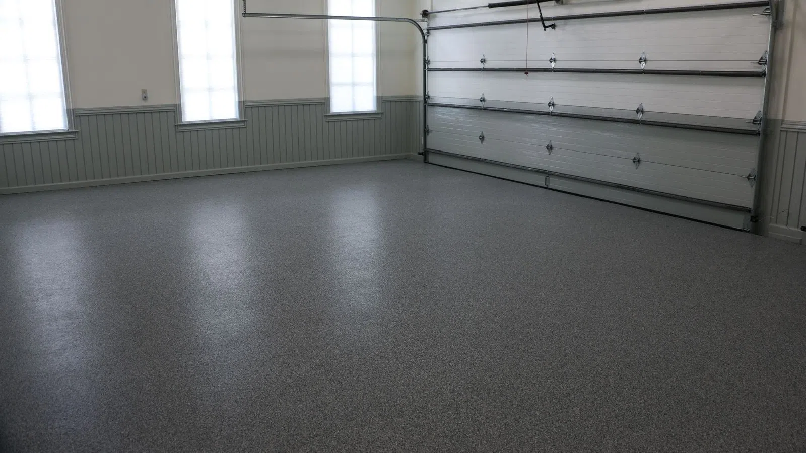 Empty clean residential garage with smooth gray epoxy floor coating and white paneled walls under natural light.