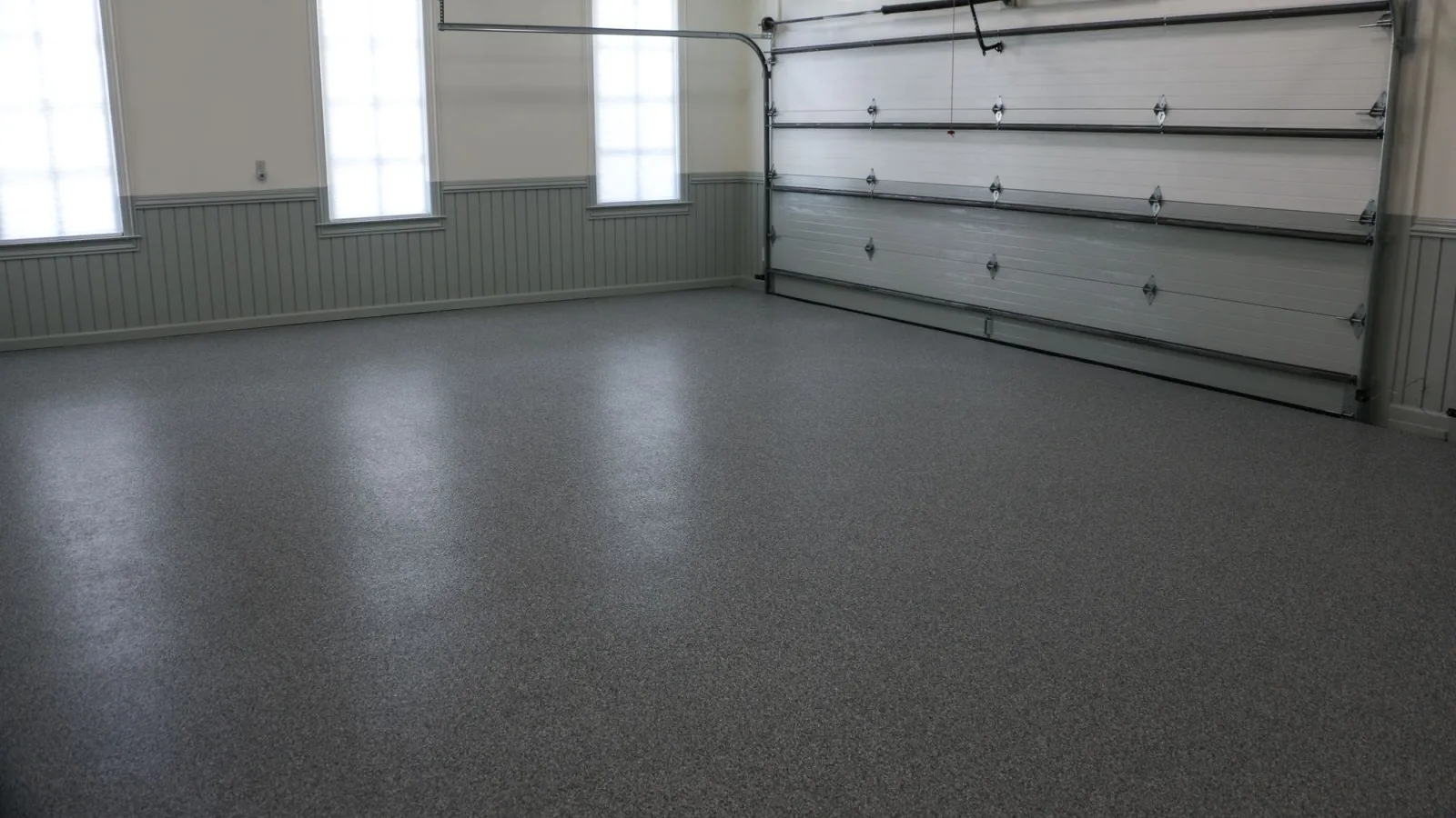 Empty garage interior with polished epoxy gray floor, white walls, large windows, and closed garage door.