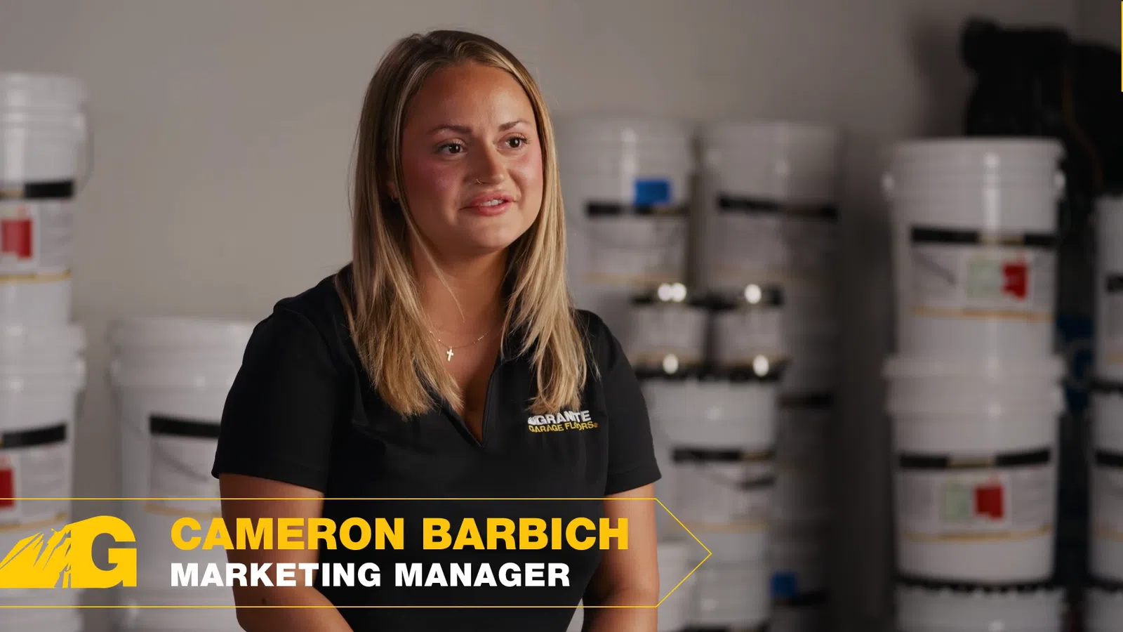 Marketing manager Cameron Barbich speaking in front of stacked white containers in a warehouse setting.