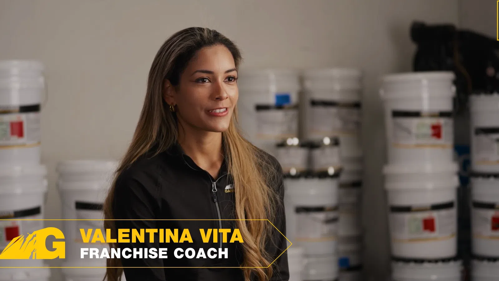 Valentina Vita, franchise coach, speaks confidently with stacked containers in the background at a franchise event.