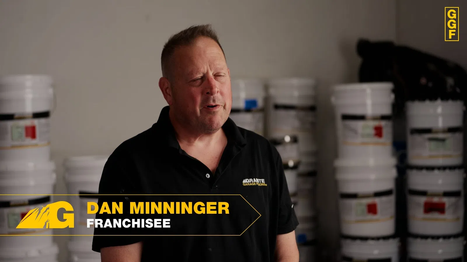 Man named Dan Minninger wearing a black shirt stands in front of stacked white buckets in a warehouse.