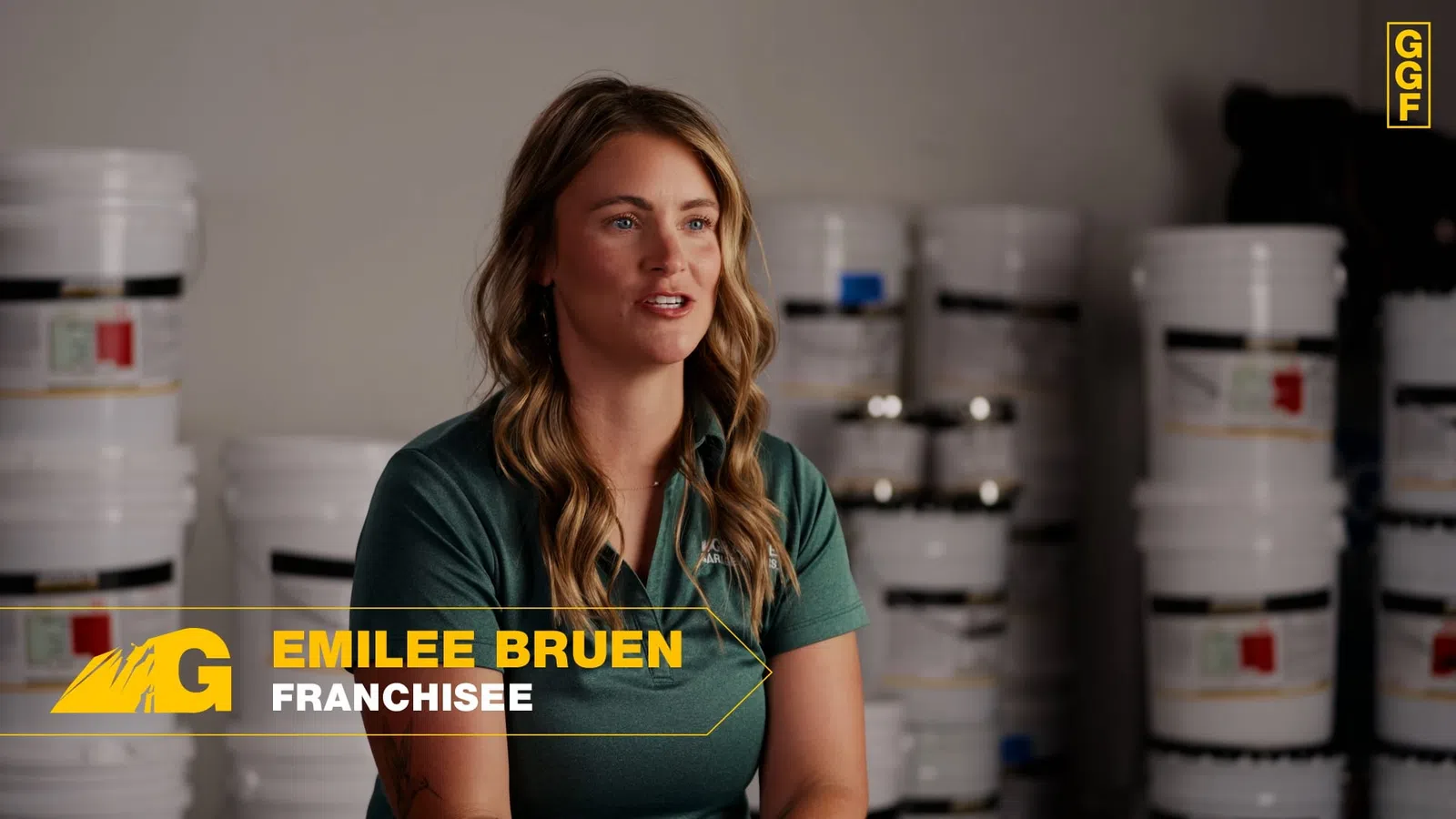 Emilee Bruen, a franchisee, speaking in a warehouse surrounded by white paint buckets and containers.