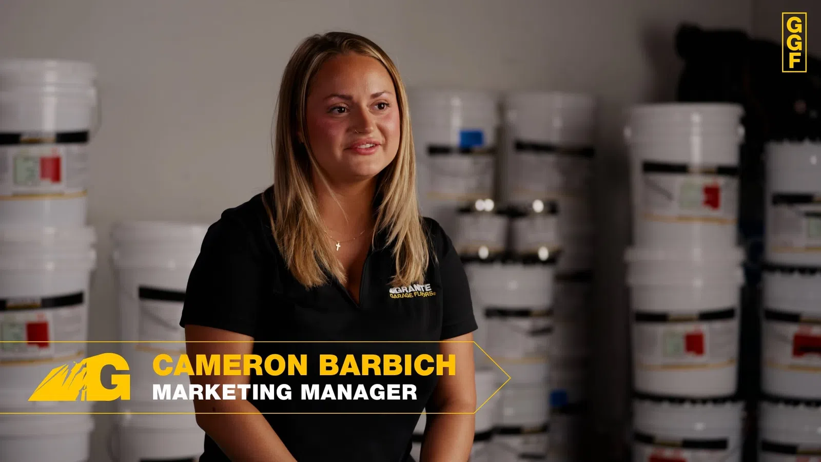 Marketing manager Cameron Barbich sitting in front of stacked white product buckets and wearing a black shirt