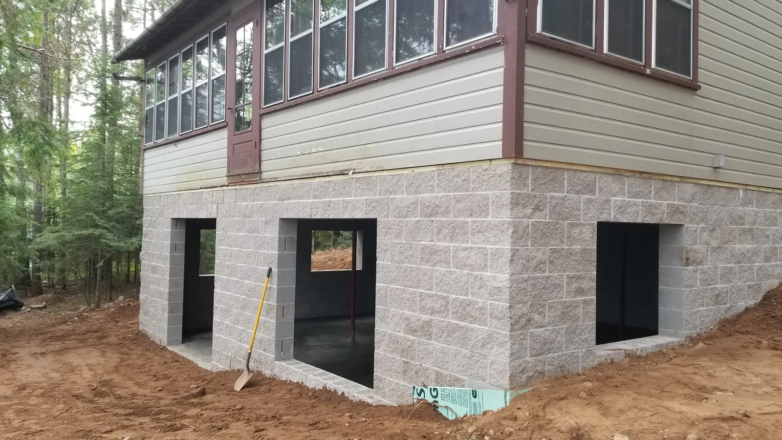 Newly constructed cabin foundation with stone masonry and large windows in a wooded area.