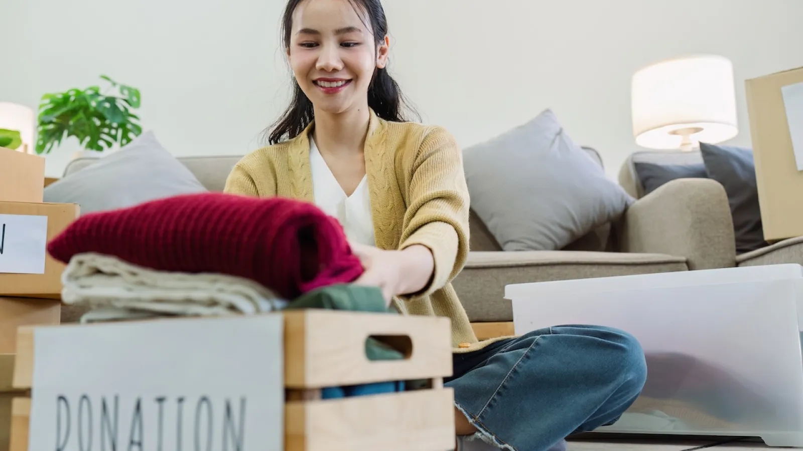 Woman organizing donations in a cozy living room, folding clothes into a donation box.