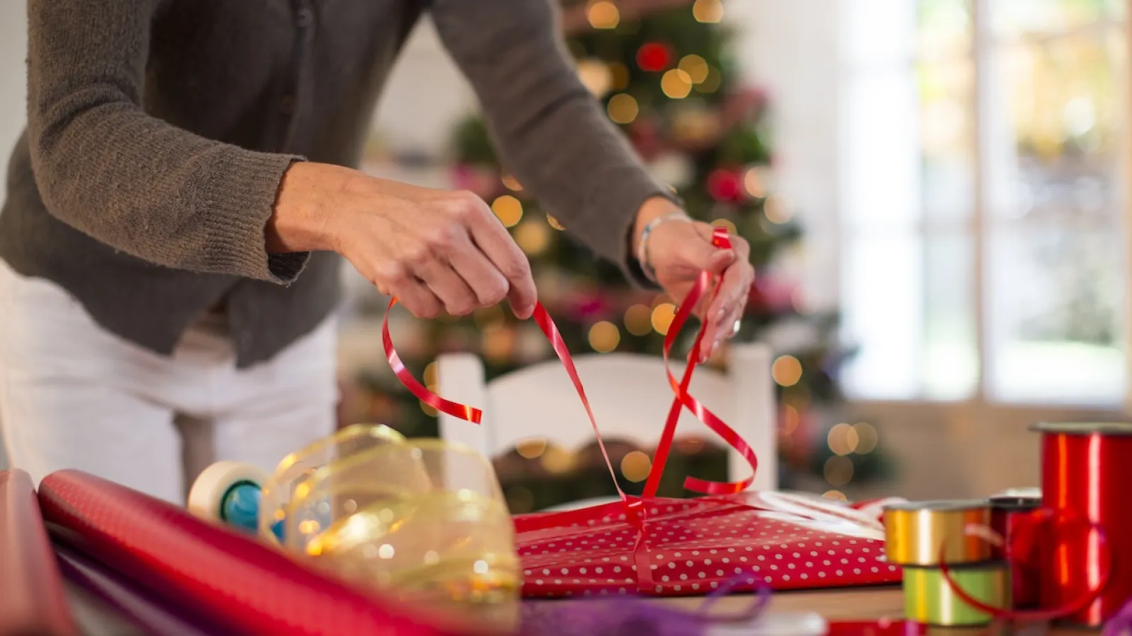 a person putting a red ribbon on a gift box