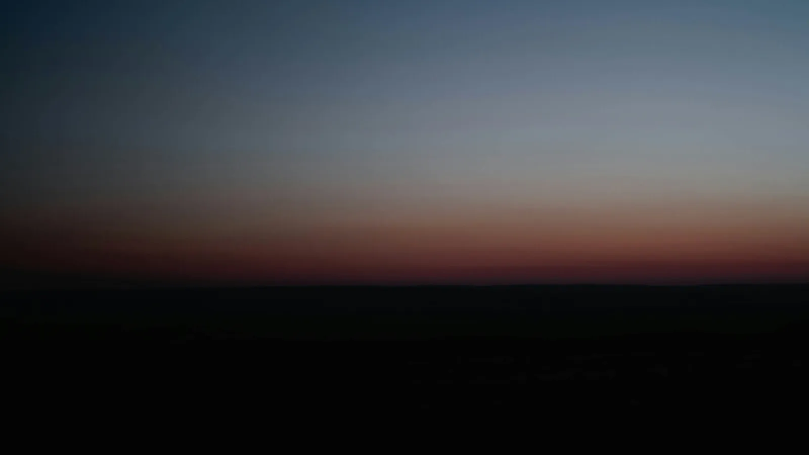 Dark landscape silhouette under a gradually fading sunset sky transitioning from orange to deep blue.