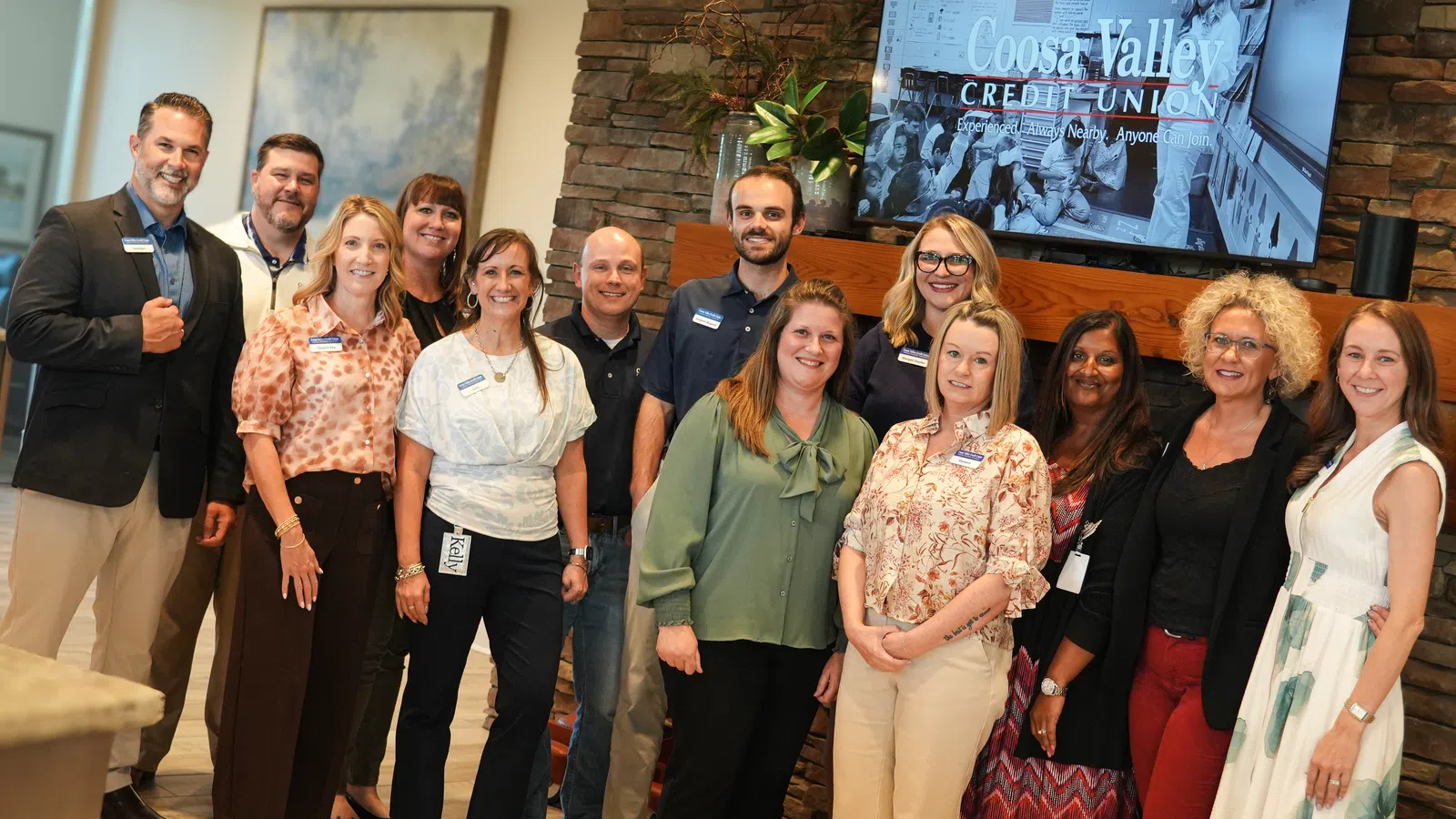 Coosa Valley Credit Union team posing in front of a stone fireplace and company sign inside office lobby.