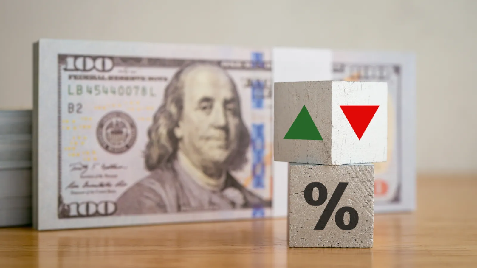 Stacked wooden blocks with arrows and percent sign in front of a US $100 bill on a wooden surface.