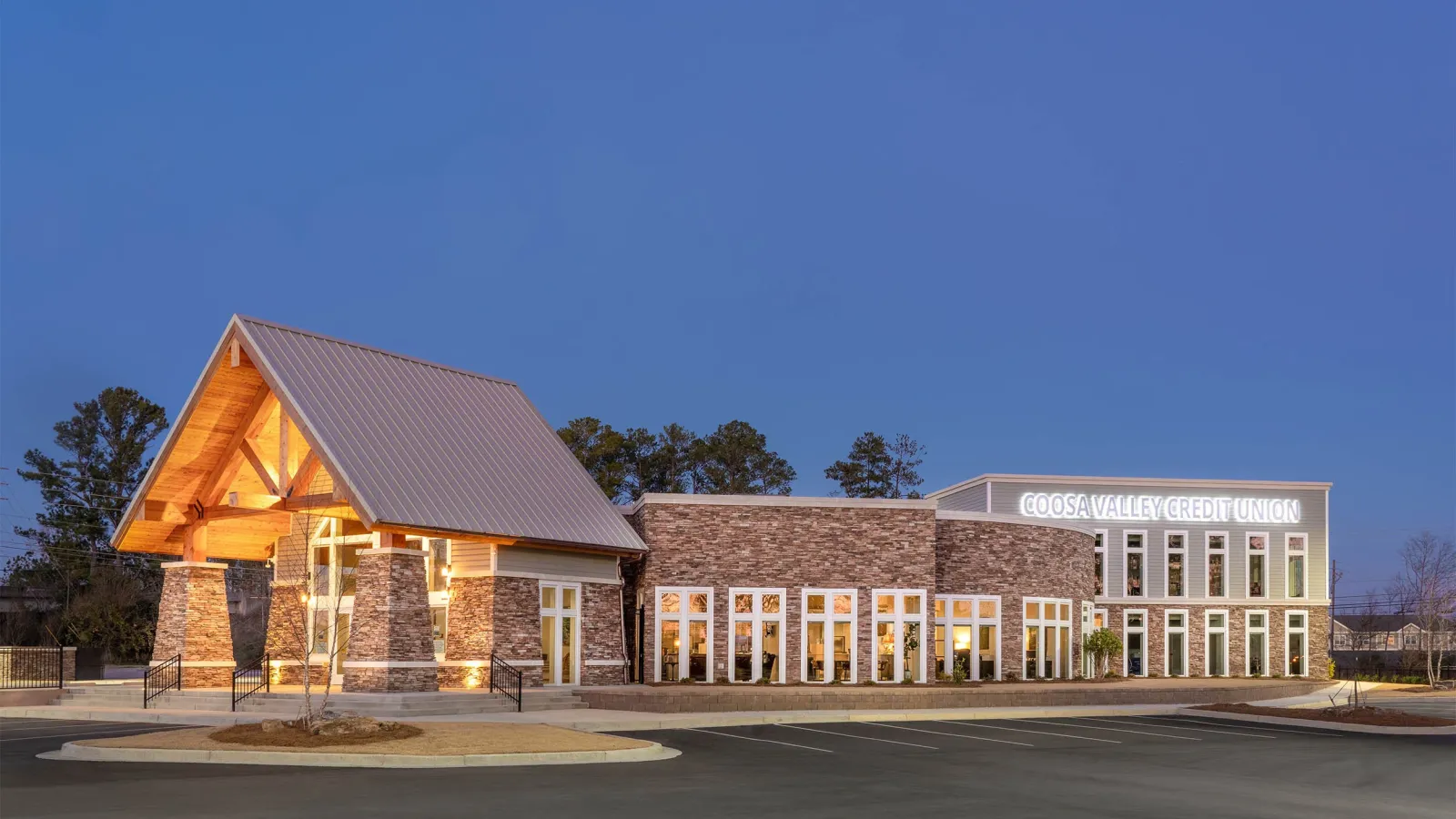 Modern Coosa Valley Credit Union building with stone facade and large windows lit at dusk under a clear blue sky