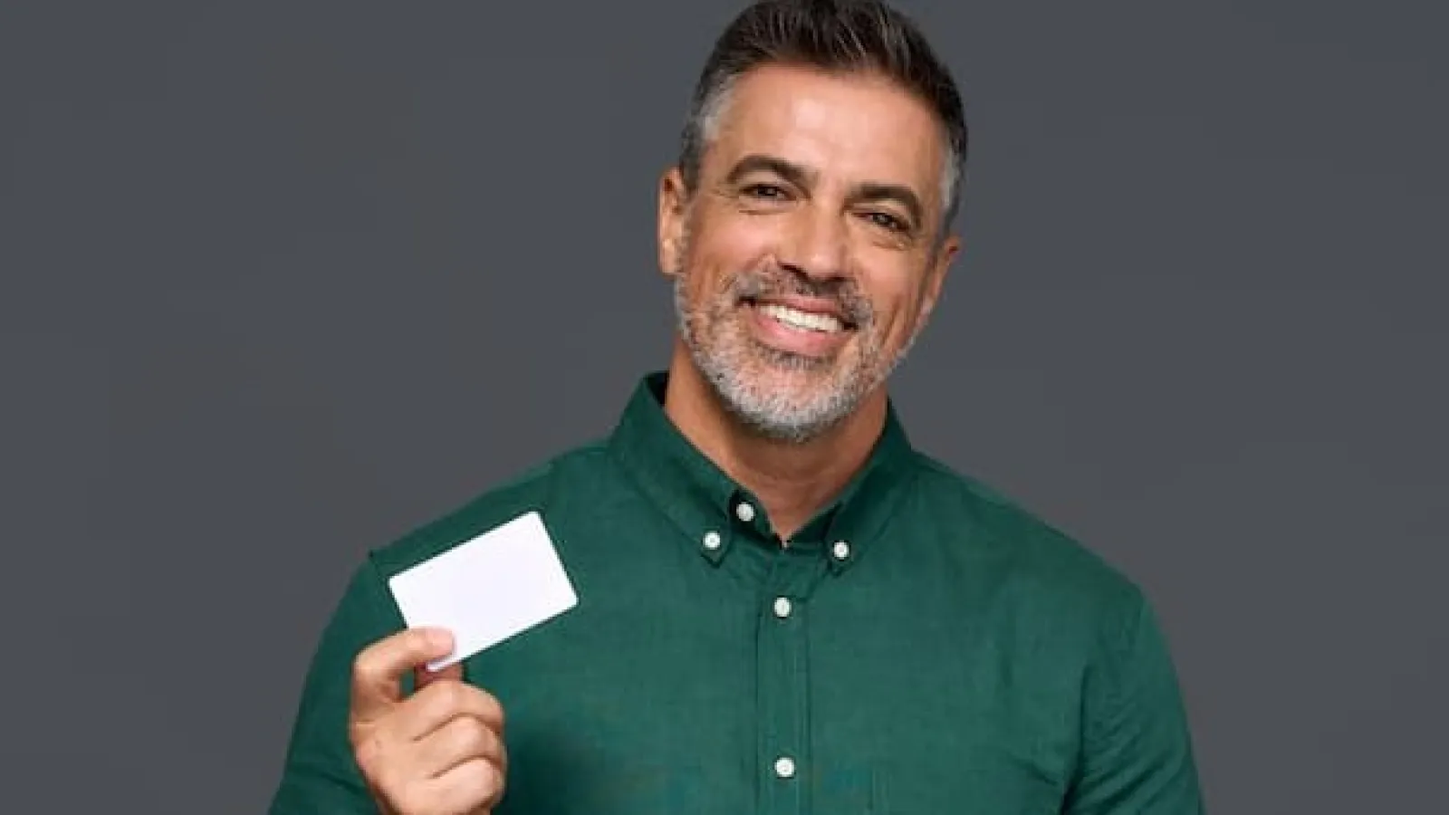 Smiling man holding a smartphone and a blank white credit card, illustrating the advantages of credit unions over banks for personal finance.