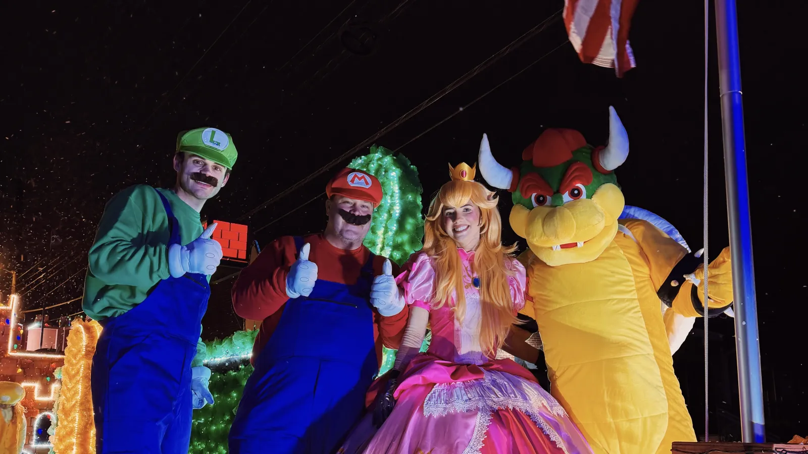 Four people dressed as Mario, Luigi, Princess Peach, and Bowser from Super Mario, posing outdoors at night.