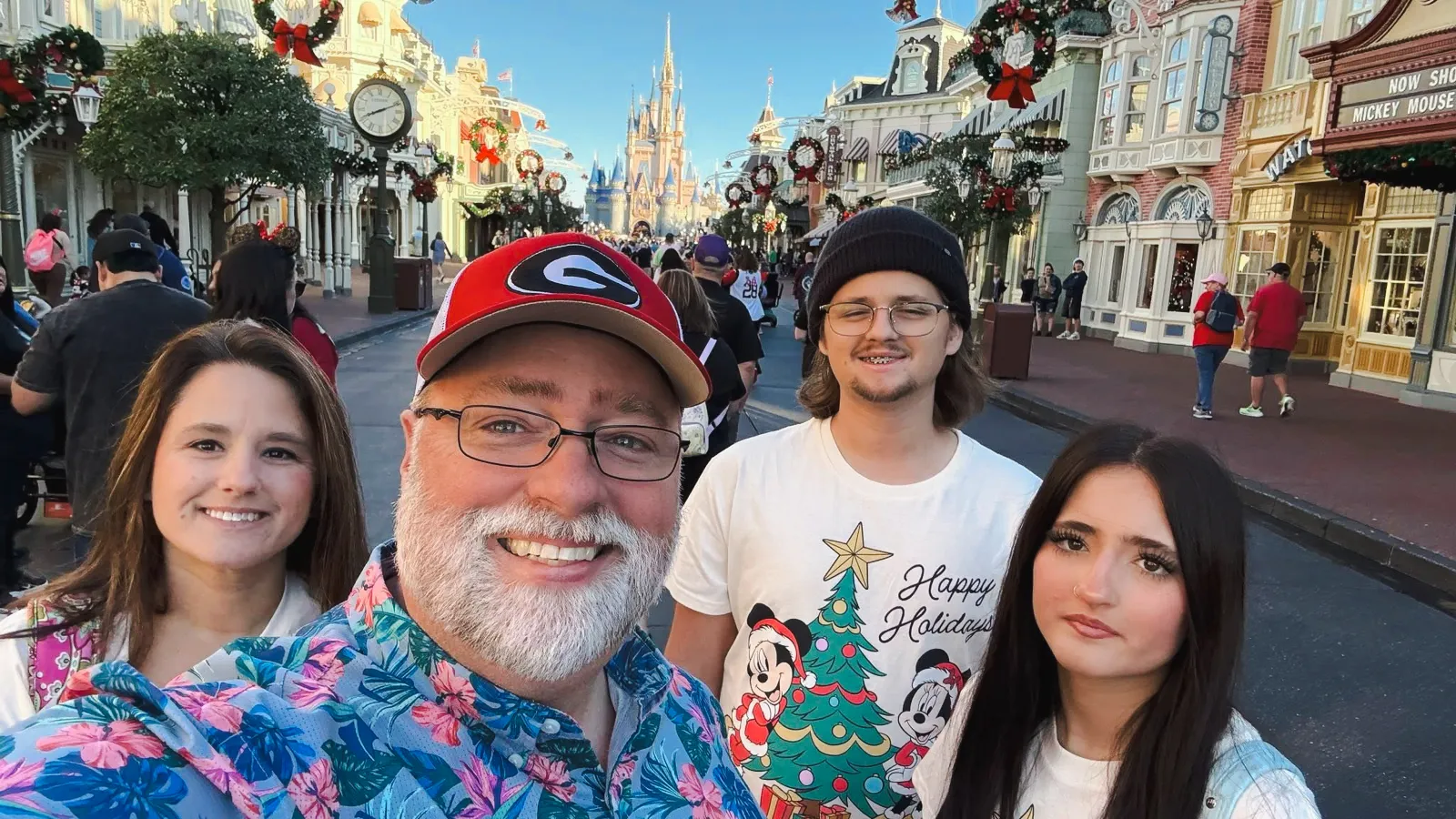 Family of four taking a selfie on a festive Main Street with holiday decorations and Cinderella castle in the background