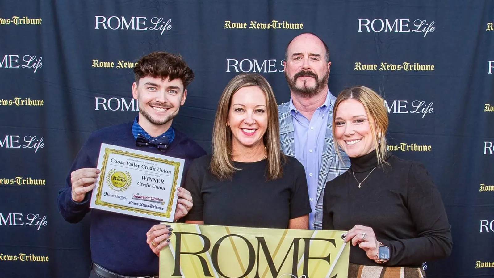 Four people posing with an award certificate and a Rome Life Best of award banner at a photo backdrop