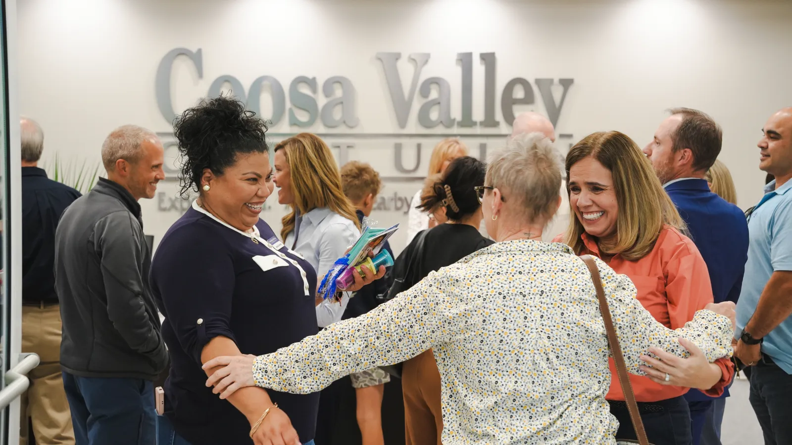People smiling and greeting each other warmly at a Coosa Valley event indoors