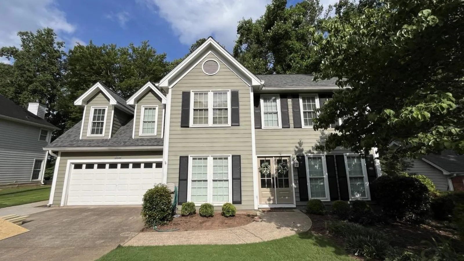 Two-story gray house with white trim, black shutters, double garage, and landscaped front yard under a blue sky.