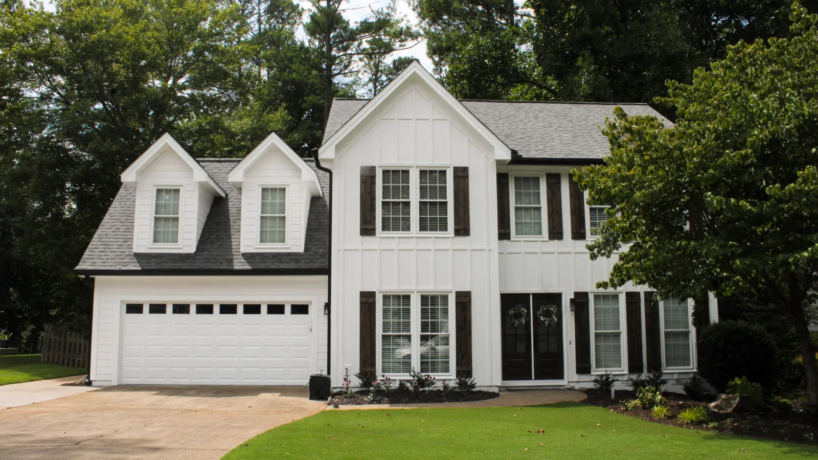 Modern two-story white house with large windows, black shutters, and a spacious driveway surrounded by green lawn.