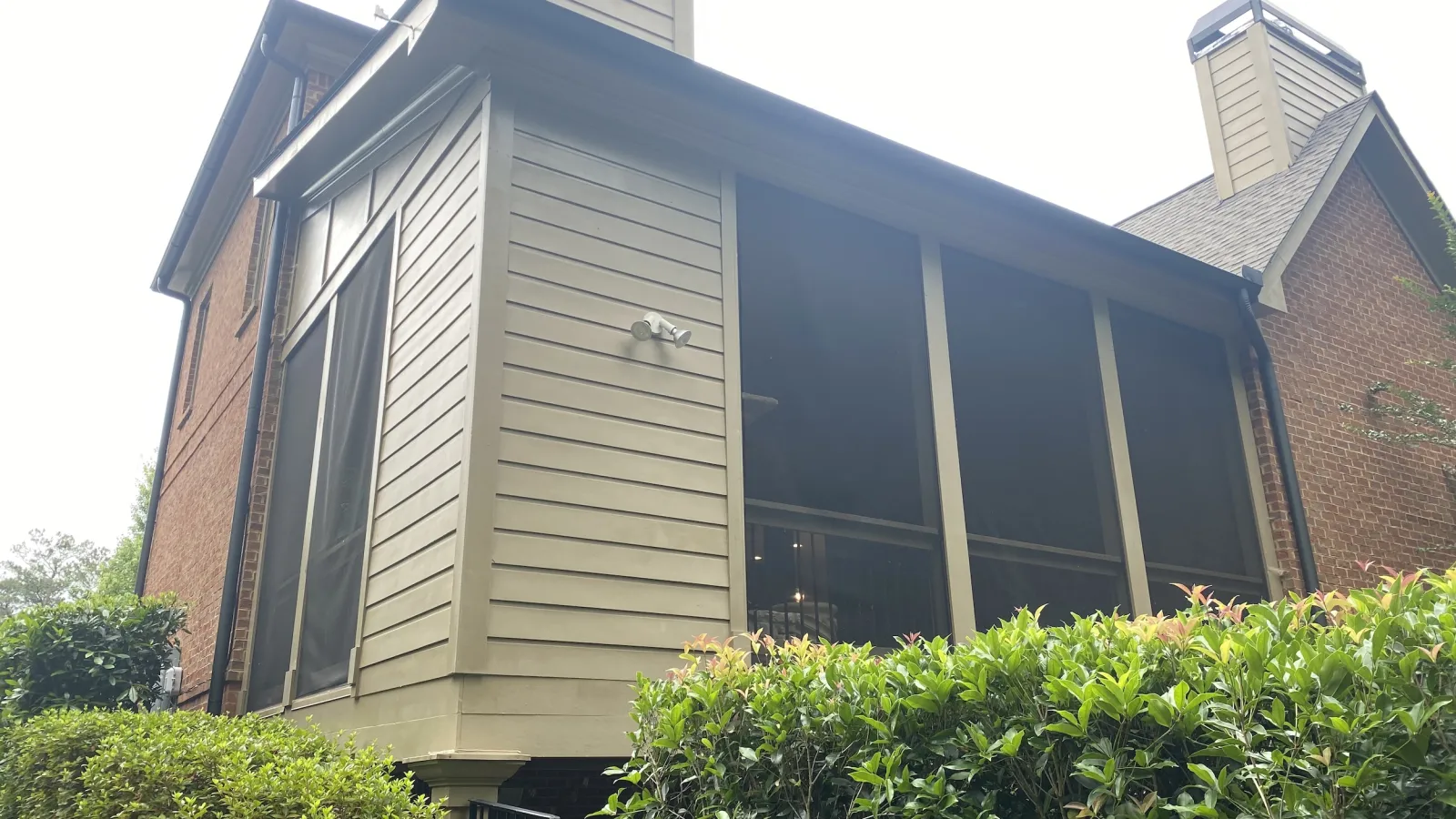 Exterior view of a two-story house with screened porch and surrounding green bushes under daylight.