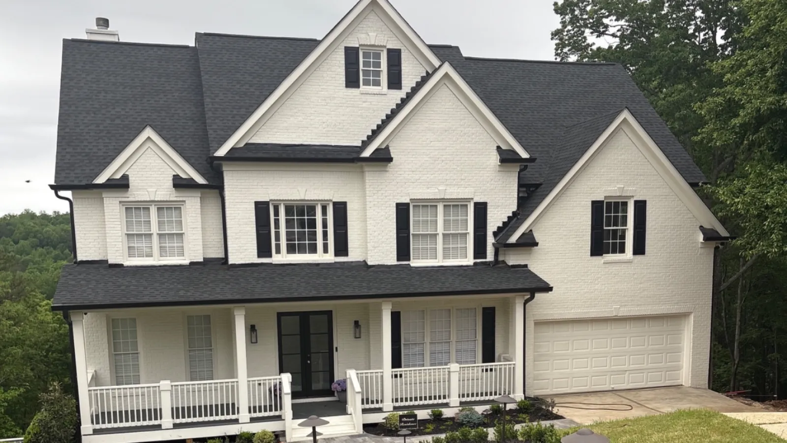 Large white two-story house with black roof and shutters, stone pathway, and manicured front yard landscape.