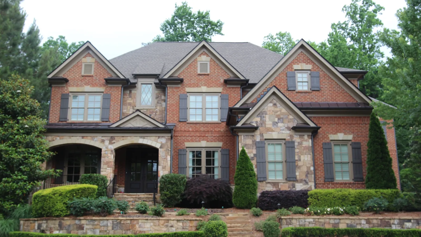 Large two-story brick and stone house with symmetrical windows, arched porch, and well-maintained landscaping